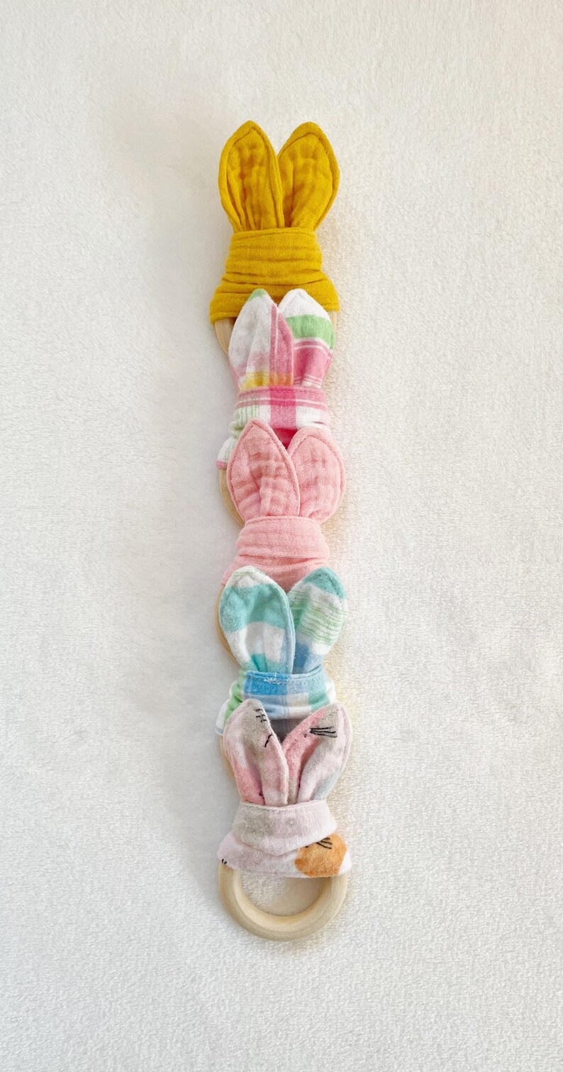 Peut inclure: Un ensemble de cinq hochets en forme de lapin de couleurs diff&eacute;rentes avec un anneau en bois. Les hochets sont faits de tissu doux et ont des motifs diff&eacute;rents, notamment du vichy rose et blanc, du vichy bleu et blanc et du jaune.