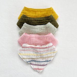 May include: Five fabric baby bibs in a stack. The top bib is yellow, the next is green, the next is light green, the next is pink, and the bottom bib is striped with pink, yellow, blue, and gray.