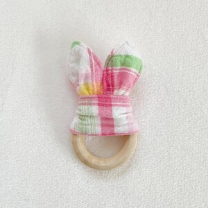 Peut inclure: Un anneau de dentition en bois recouvert d'un tissu &agrave; carreaux rose et vert. Le tissu est nou&eacute; en oreilles de lapin.