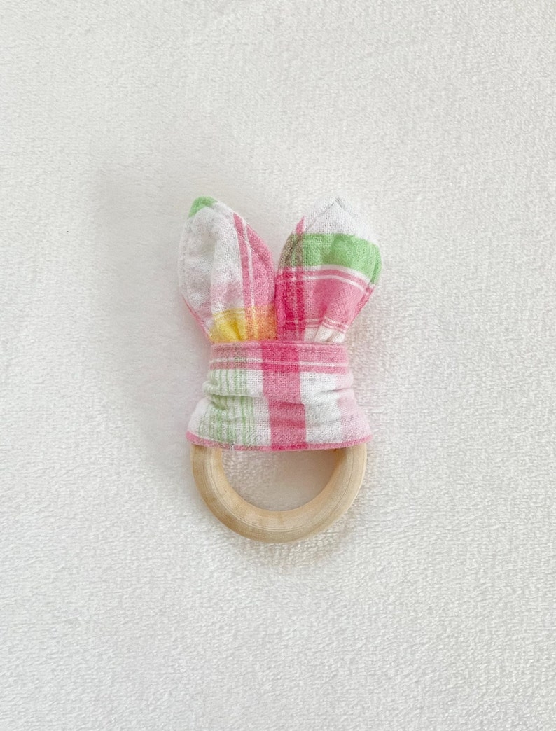 Peut inclure: Un anneau de dentition en bois recouvert d'un tissu &agrave; carreaux rose et vert. Le tissu est nou&eacute; en oreilles de lapin.