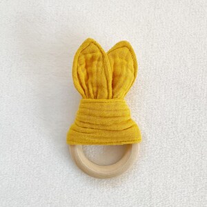 Peut inclure: Un anneau de dentition en tissu jaune en forme de lapin avec un anneau en bois. L'anneau de dentition est fait d'un tissu doux et textur&eacute; et est con&ccedil;u pour que les b&eacute;b&eacute;s puissent le m&acirc;cher.