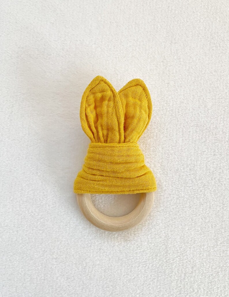 Peut inclure: Un anneau de dentition en tissu jaune en forme de lapin avec un anneau en bois. L'anneau de dentition est fait d'un tissu doux et textur&eacute; et est con&ccedil;u pour que les b&eacute;b&eacute;s puissent le m&acirc;cher.