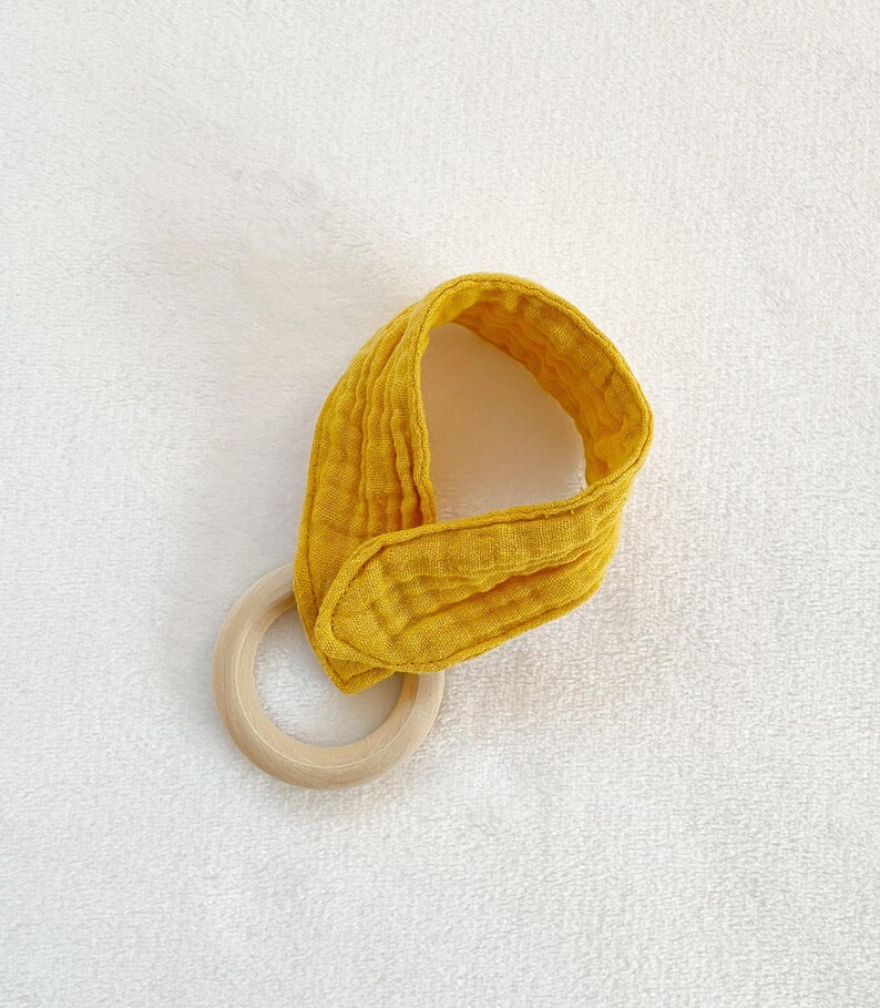 Peut inclure: Un anneau de dentition pour b&eacute;b&eacute; en tissu jaune avec un anneau en bois. Le hochet est fait d'un tissu doux et textur&eacute; et est con&ccedil;u pour que les b&eacute;b&eacute;s puissent m&acirc;cher.