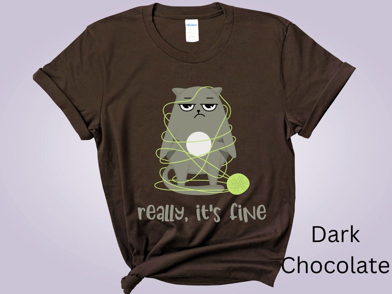 May include: Dark chocolate brown t-shirt featuring a grumpy gray cat tangled in green yarn. The text "really, it's fine" is below the cat. A green ball of yarn is on the right. The shirt is a Gildan brand.