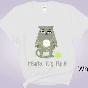 May include: White t-shirt featuring a grumpy gray cat tangled in green yarn with a matching ball of yarn. The text "really, it's fine" is printed below the cat. The shirt is a Gildan brand.