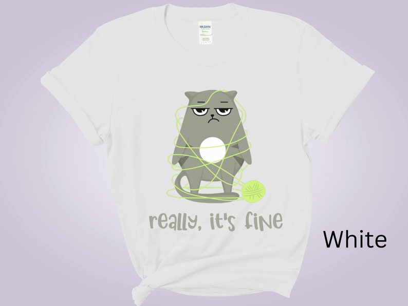 May include: White t-shirt featuring a grumpy gray cat tangled in green yarn with a matching ball of yarn. The text "really, it's fine" is printed below the cat. The shirt is a Gildan brand.