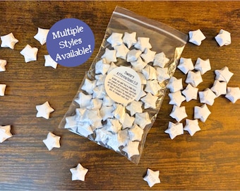 May include: A clear plastic bag filled with small white paper stars, each featuring printed text. A circular label on the bag reads Sweary Affirmations 2.0. A purple circular graphic with the text Multiple Styles Available is included.