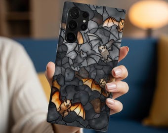 May include: A phone case featuring a stained-glass design with bats. The bats have orange and white wings, set against a dark gray background. The case has a glossy finish and a multi-lens camera.