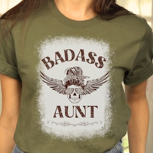 May include: A green t-shirt with a white distressed graphic that says "Badass Aunt" with a skull wearing sunglasses and wings.