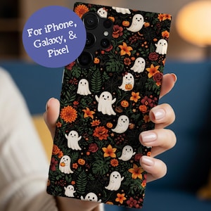 May include: A rectangular phone case featuring a black background with a repeating pattern of white ghosts, orange pumpkins, and various orange and red flowers with green foliage. A purple circular graphic contains the text For iPhone, Galaxy, & Pixel.