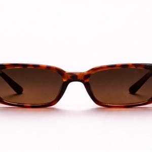 May include: Tortoiseshell sunglasses with brown lenses. The rectangular frames have rounded edges and a classic tortoiseshell pattern. The lenses are a solid brown color, providing shade and style.