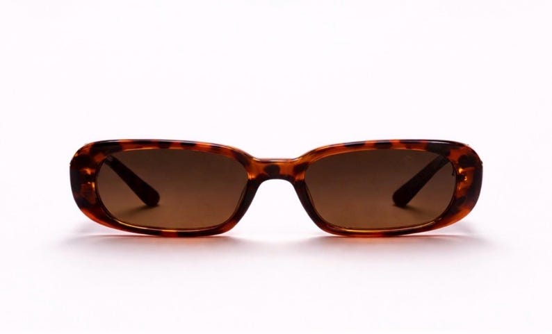 May include: Tortoiseshell sunglasses with brown lenses. The rectangular frames have rounded edges and a classic tortoiseshell pattern. The lenses are a solid brown color, providing shade and style.