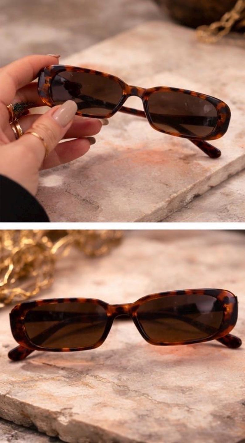 May include: Rectangular sunglasses with a tortoiseshell pattern. The frames are brown with dark lenses. The sunglasses are shown on a textured surface.