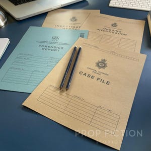 May include: A collection of paper folders including a blue Forensics Report and tan Central Division Police Case File, Ongoing Investigation, and Investigation Report documents, with two dark pencils resting on the top tan folder.