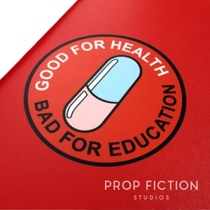 May include: A red sticker with a black circle around the words "Good for Health Bad for Education" and a cartoon pill in the centre. The text "Prop Fiction Studios" is below the sticker.