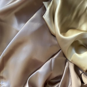 Peut inclure: Gros plan sur un tissu drapé dans des tons or et champagne. Le satin a un éclat brillant, avec des plis et des reflets doux. L'image met en valeur la texture et les variations de couleur du tissu.