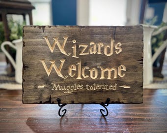 May include: A wooden sign with the words "Wizards Welcome" carved into it. The sign also has the words "Muggle tolerated" carved into it.