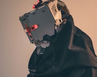 May include: A person wearing a black hooded jacket with a silver and red metal helmet. The helmet has a cross-shaped design and a red light on top.