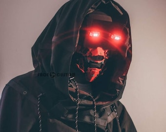 May include: A person wearing a black hooded jacket with a red and black mask. The mask has glowing red eyes.