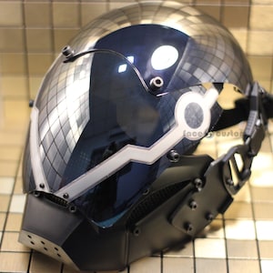 May include: A black and silver helmet with a clear visor and a white light strip. The helmet has a strap and multiple screws. The helmet is reflecting the surrounding environment.
