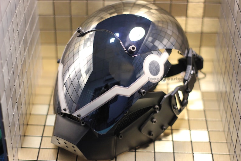 May include: A black and silver helmet with a clear visor and a white light strip. The helmet has a strap and multiple screws. The helmet is reflecting the surrounding environment.