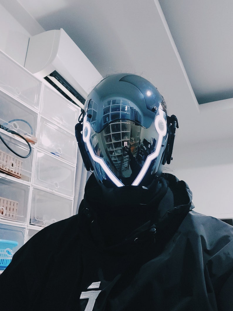 May include: A black helmet with a reflective visor and white LED lights around the edges. The helmet has a futuristic design.