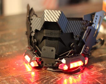 May include: A black motorcycle helmet with a carbon fiber design and red LED lights. The helmet has a built-in rear light and a rear brake light.