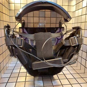 May include: A black and gray face mask with a clear visor and adjustable straps. The mask has a black battery pack attached to the side.
