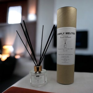 May include: A gold tube with a white label that reads "SIMPLY MELTED Reed Diffuser Vegan-Friendly Diffuser Base Oil Vegan Friendly and Cruelty Free Fragrance Oil". A clear glass bottle with a gold lid and black reeds is in front of the tube.