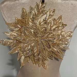 Puede incluir: Una aplicación floral dorada y marfil con adornos de perlas y lentejuelas. La aplicación es perfecta para añadir un toque de elegancia a la ropa, los accesorios o la decoración del hogar.