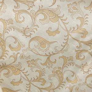 May include: A white fabric with a beige paisley pattern. The pattern features intricate swirls and floral motifs.