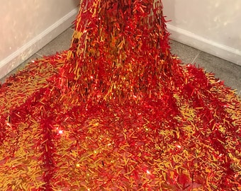 Könnte beinhalten: Roter und goldener Paillettenstoff mit Fransenmuster. Der Stoff ist über eine Schaufensterpuppe drapiert.