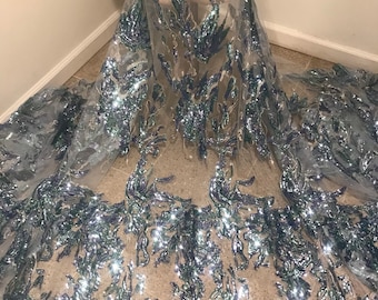 May include: Silver and blue sequined lace fabric with a floral design. The fabric is sheer and has a delicate texture.