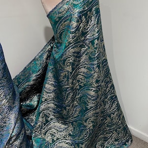 May include: Teal fabric with a gold metallic paisley pattern. The fabric is draped over a dress form.