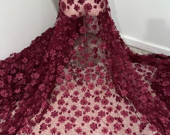 May include: Burgundy floral lace fabric with 3D flowers and pearl embellishments. The lace has a scalloped edge.
