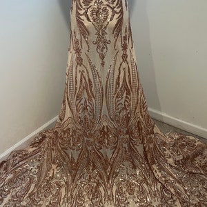 Puede incluir: Tela de lentejuelas de color oro rosa con un patrón floral. La tela es transparente y tiene un tacto delicado y femenino.