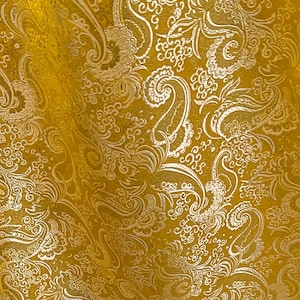May include: Gold fabric with a white paisley pattern. The fabric has a shiny, metallic finish.
