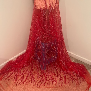 May include: A vibrant red fabric with intricate, swirling patterns and sparkling embellishments. The sheer material drapes elegantly, showcasing a detailed design. This textile is suitable for creating dresses, skirts, or other apparel.
