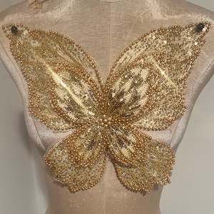 May include: A gold butterfly applique with pearl accents. The butterfly is made of sequins and mesh fabric.