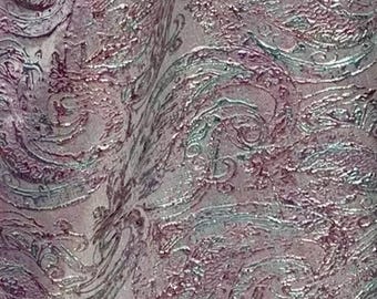May include: Close-up of a pink and silver fabric with a paisley pattern. The fabric has a textured, embossed look.