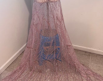Könnte beinhalten: Ein durchsichtiger, hellrosa Stoff mit aufwendigen Pailletten- und Glitzermustern. Der Stoff ist über eine Schaufensterpuppe drapiert und zeigt sein fließendes Design. Das Design weist vertikale und geometrische Muster auf, die einen schimmernden Effekt erzeugen, ideal für formelle Kleidung.