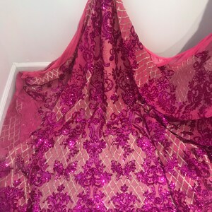 Op de afbeelding: Roze en gouden paillettenstof met een bloemenpatroon. De stof is doorschijnend en heeft een delicate, vrouwelijke uitstraling.
