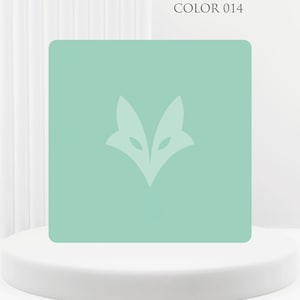 Peut inclure: Un carreau carré vert menthe présentant un graphique stylisé de tête de renard centré dans une teinte de vert plus clair. Le texte COLOR 014 est imprimé dans le coin supérieur droit. Le carreau a des coins arrondis et une finition mate.