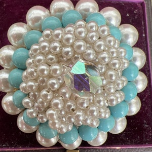 May include: A brooch made of white and light blue pearls with a clear iridescent crystal in the center.