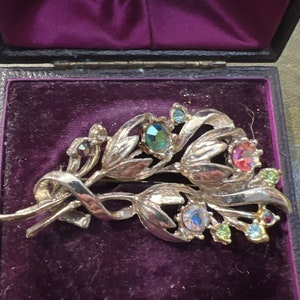 Puede incluir: Un broche de plata en forma de ramo de flores con pedrería multicolor. El broche se muestra en una caja forrada de terciopelo.