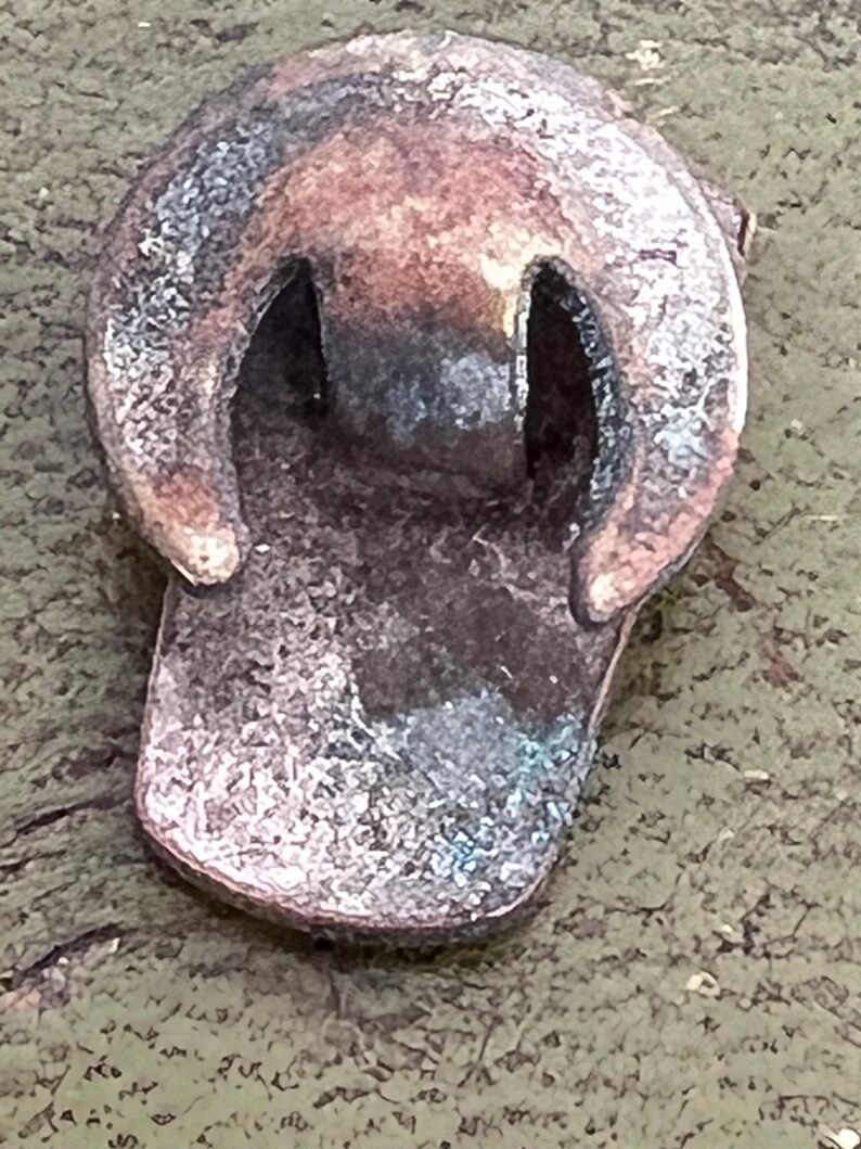 May include: Close-up of a weathered, metallic object with a rounded top and a rectangular base. The object has two arched openings and a distressed, aged appearance with shades of brown, copper, and hints of blue-green. The texture appears rough and worn.