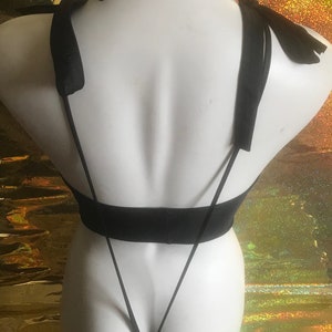 May include: Black lingerie with thin straps and a tie-back design. The straps are tied into bows at the shoulders.