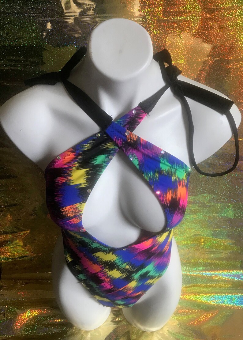 May include: A colorful, abstract print bodysuit with a criss-cross halter neckline and rhinestones. The bodysuit has a cutout at the chest and a high-cut leg.