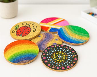 Può includere: Una collezione di sottobicchieri rotondi in sughero con disegni colorati. Uno presenta una coccinella, mentre altri mostrano motivi arcobaleno, geometrici e mandala. I sottobicchieri sono progettati per bevande e per proteggere le superfici.