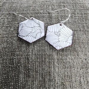 May include: A pair of silver earrings with hexagonal white ceramic pendants featuring a black and white geometric pattern.